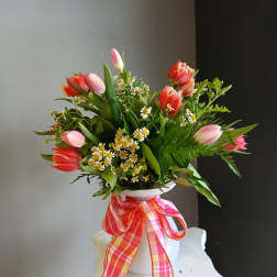 Pink and coral tulips arranged in a white vase with a plaid ribbon