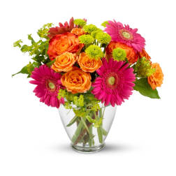 Bright bouquet of orange roses, pink gerbera daisies, and green mums in a clear glass vase