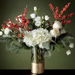 White flowers and red berry branches in a glass vase with a gold base