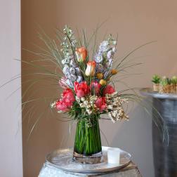 Tall floral arrangement with pink and peach blooms in a glass vase