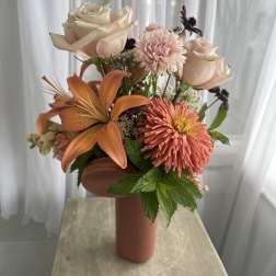 Peach and cream floral arrangement in a tall vase with roses and lilies