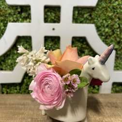 Pink and peach flowers arranged in a unicorn-shaped ceramic planter