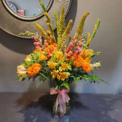 Orange and yellow mixed bouquet in a glass vase with a pink ribbon