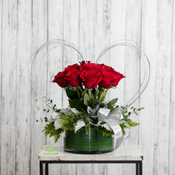 Red roses in a green vase with a silver ribbon and wire heart frame