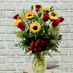 Red roses and yellow sunflowers in a glass vase with a red ribbon