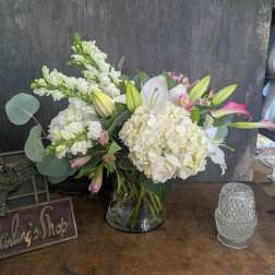 White lilies and hydrangeas in a glass vase with pink accents