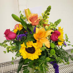Mixed bouquet with sunflowers, roses, lilies, and snapdragons in a glass vase