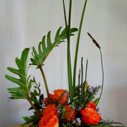 Orange roses in a green bowl with tall tropical leaves