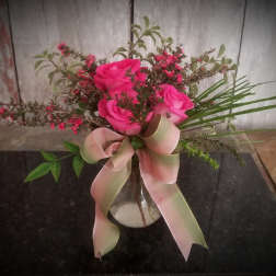 Pink roses in a clear vase with a large pale ribbon bow