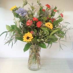 Mixed bouquet of sunflowers, red carnations, and purple blooms in a glass vase