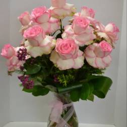 Pink-tipped roses arranged in a clear glass vase with a pink ribbon