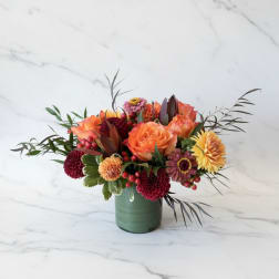Orange and burgundy floral arrangement in a green vase