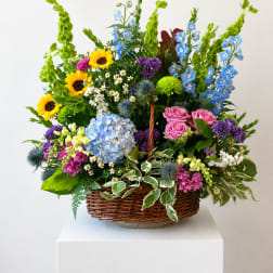 Mixed flower basket with sunflowers, blue hydrangea, pink roses, and purple blooms