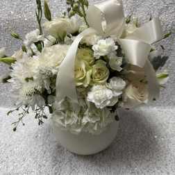 White floral arrangement with roses, carnations, and a satin ribbon in a vase