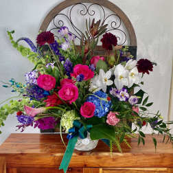Colorful mixed flower arrangement in a white container with a teal ribbon