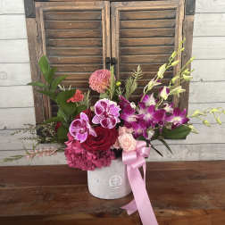 Pink and purple floral arrangement in a white vase with a pink ribbon