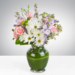 Mixed bouquet of white daisies, pink carnations, and lavender flowers in a green glass vase