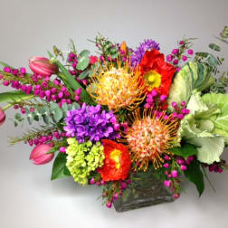 Colorful mixed bouquet in a square glass vase with pink tulips and purple blooms