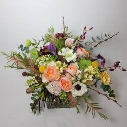 Mixed bouquet with peach, white, purple, and yellow flowers in a glass vase
