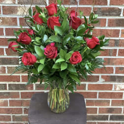 Red roses arranged in a clear glass vase with greenery