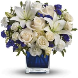 White lilies and roses with blue accents in a cobalt glass cube vase