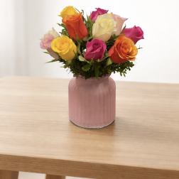 Mixed roses in a pink glass vase on a wooden table