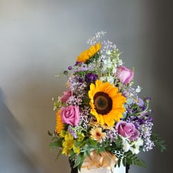 Mixed bouquet with sunflowers, pink roses, and purple flowers in a white box