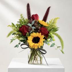 Bouquet of red roses and sunflowers in a glass vase with a striped ribbon