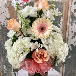 Peach roses and white flowers in a green vase with a pink ribbon