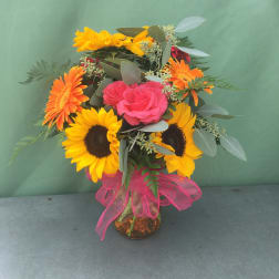 Bouquet of sunflowers, pink roses, and orange gerbera daisies in a glass vase