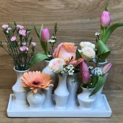 Floral arrangement in white bud vases with pink tulips, roses, and a peach gerbera daisy