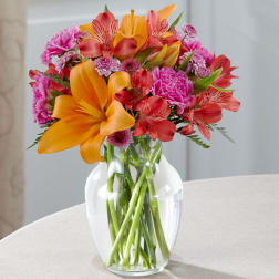 Bouquet of orange lilies, pink alstroemeria, and magenta carnations in a clear glass vase