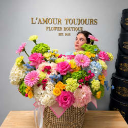 Large mixed flower arrangement in a woven basket with pink ribbon