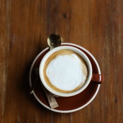 Cup of cappuccino on a saucer with a spoon on a wooden table