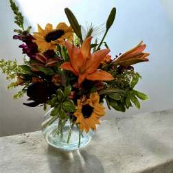 Bouquet of orange lilies and sunflowers in a clear glass vase