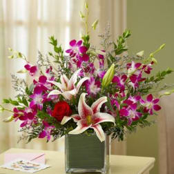 Bouquet of pink orchids, lilies, and a red rose in a square vase