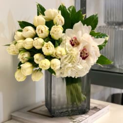 White tulips, hydrangeas, and an orchid arranged in a tall gray glass vase.
