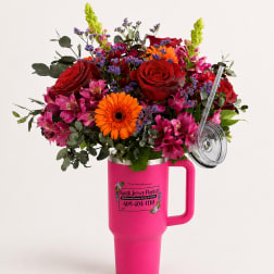 Mixed bouquet of red roses, orange gerbera daisies, and pink flowers in a pink tumbler vase