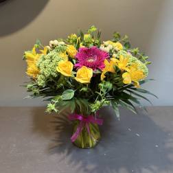 Bouquet of yellow roses and lilies with a pink gerbera in a glass vase