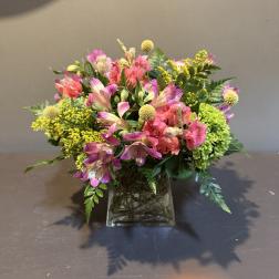Mixed pink and yellow flowers arranged in a square glass vase