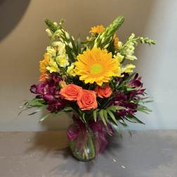 Mixed bouquet with orange roses, yellow daisies, and purple flowers in a glass vase