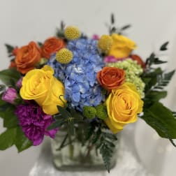 Colorful bouquet with roses, hydrangea, and purple blooms in a glass vase
