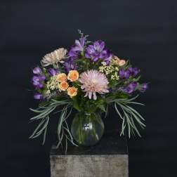 Mixed bouquet of purple, peach, and pink flowers in a glass vase