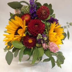 Mixed bouquet with sunflowers, purple blooms, and red dahlias in a glass vase
