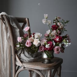 Pink and white flowers arranged in a silver vase on a wooden chair