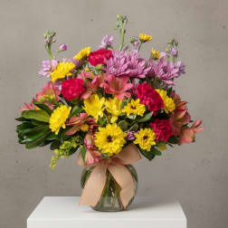 Mixed bouquet of pink, yellow, and purple flowers in a glass vase with a ribbon