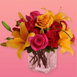 Pink and yellow flower arrangement in a clear square vase
