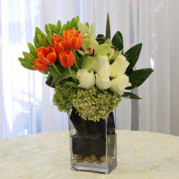 Orange tulips and white roses in a tall glass vase