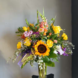Mixed bouquet with sunflowers, yellow roses, and purple flowers in a glass vase