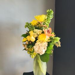 Yellow mixed flower arrangement in a tall glass vase